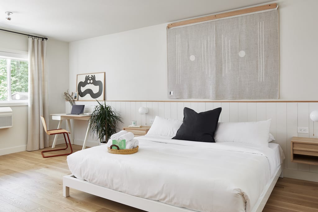Guest room with a king bed, woven wall hanging, wood desk and a basket of rolled towels