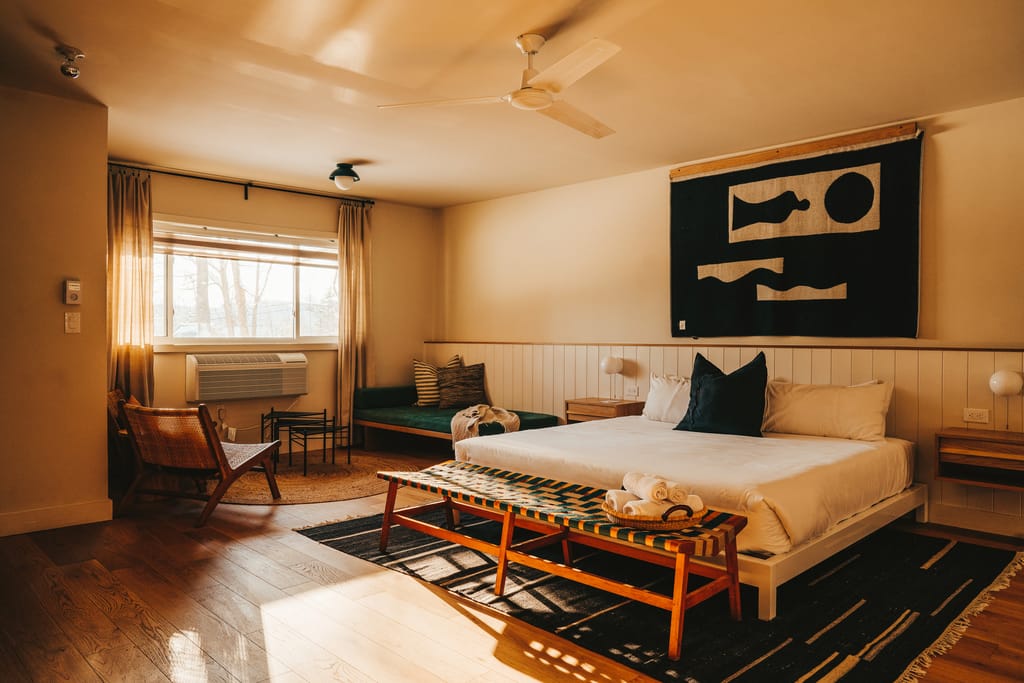 Bedroom with a king bed, a woven bench with rolled towels and a large black and cream wall hanging