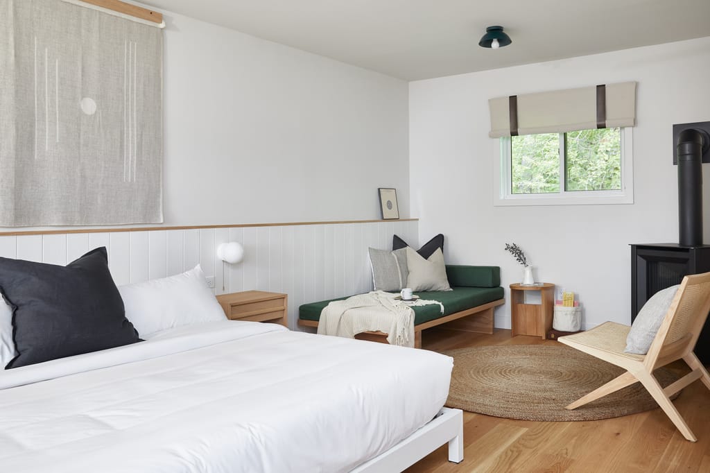 Guest room with a made bed, green daybed, round jute rug, rattan chair and gas stove