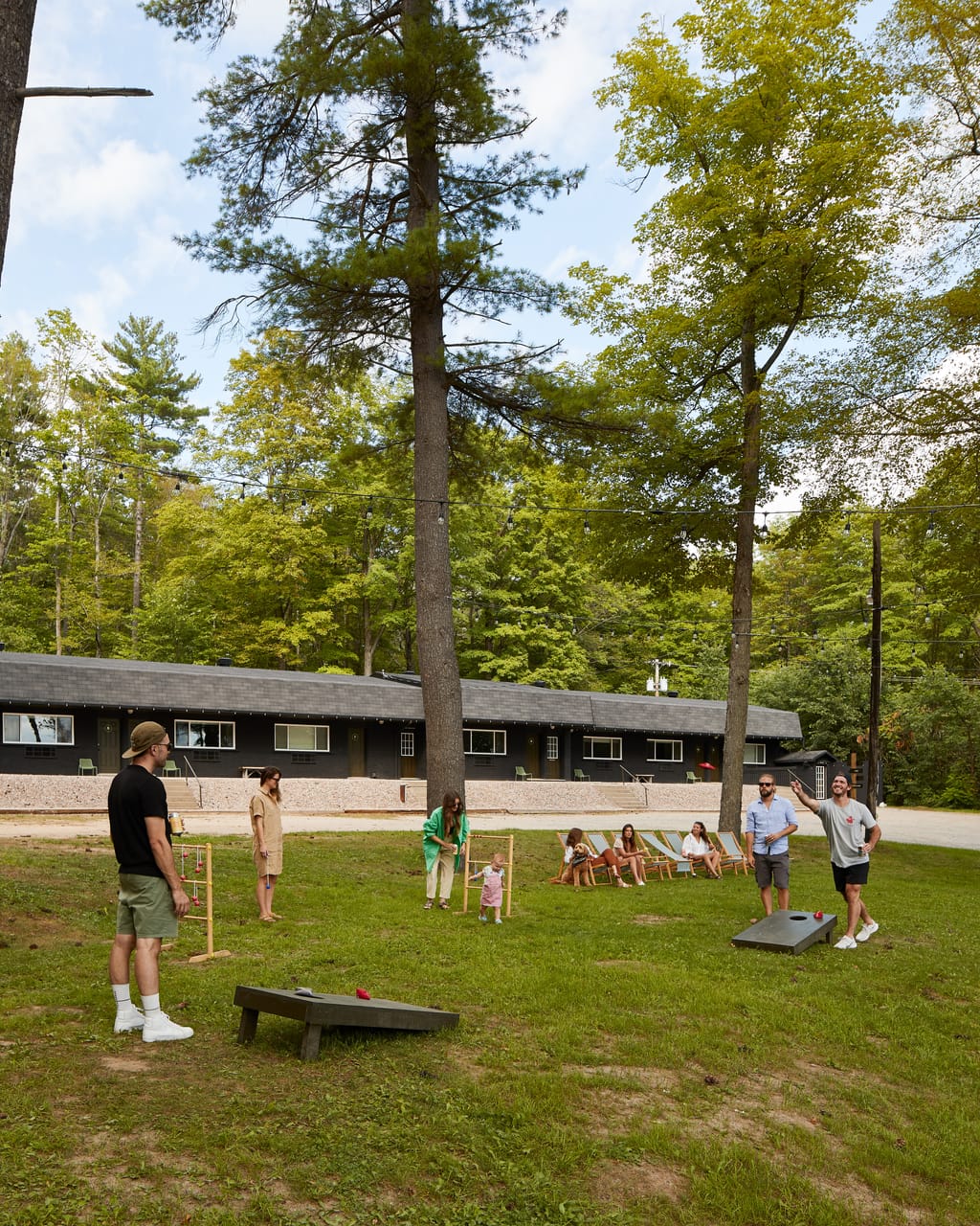 Guests playing cornhole and ladder toss on the lawn in front of the low black boutique motel at Somewhere Inn Calabogie