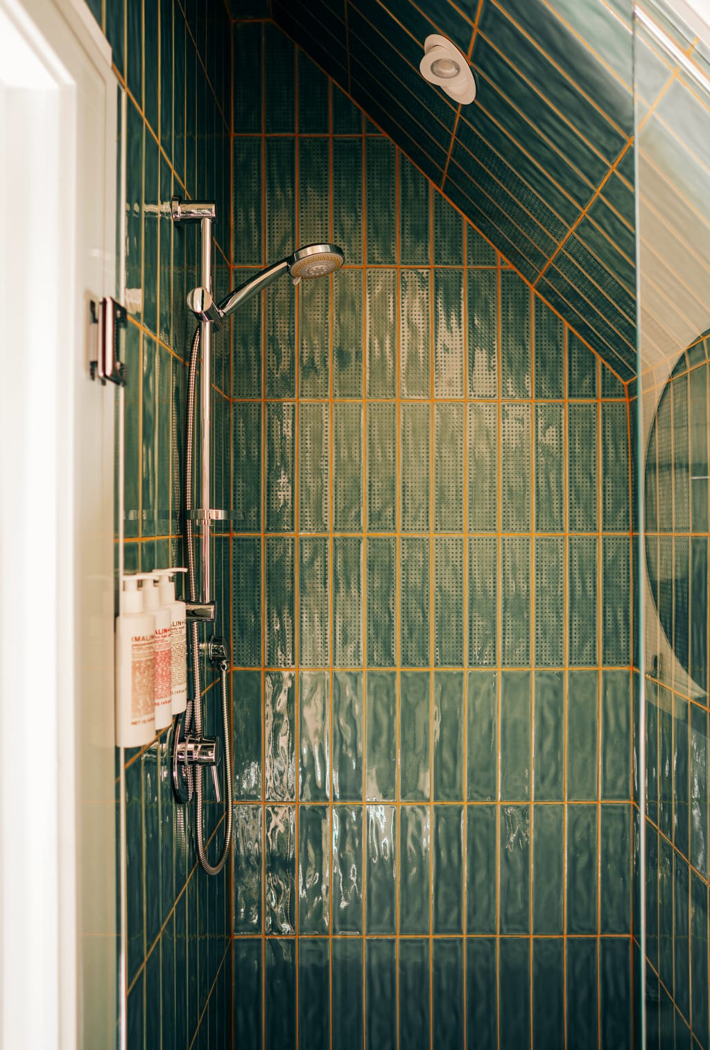 Shower with green glazed tile, a handheld shower head and wall-mounted toiletries