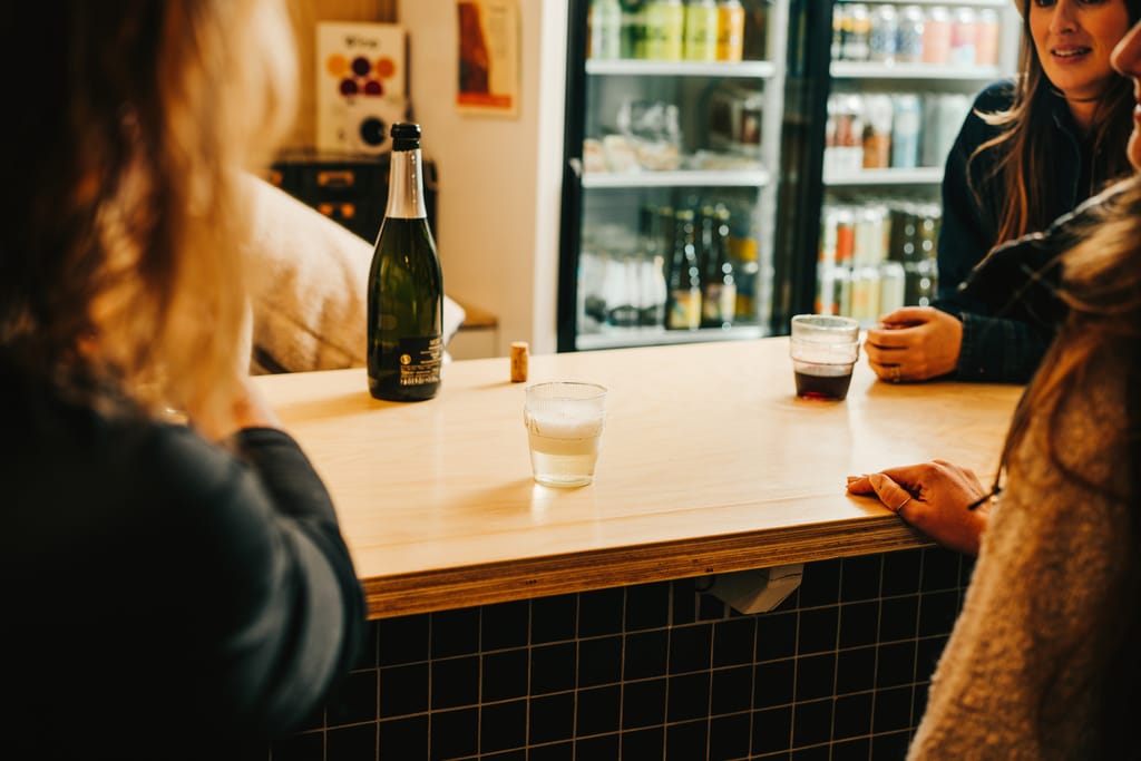 Bar counter with an open bottle of sparkling wine, a cork and glasses, guests on either side