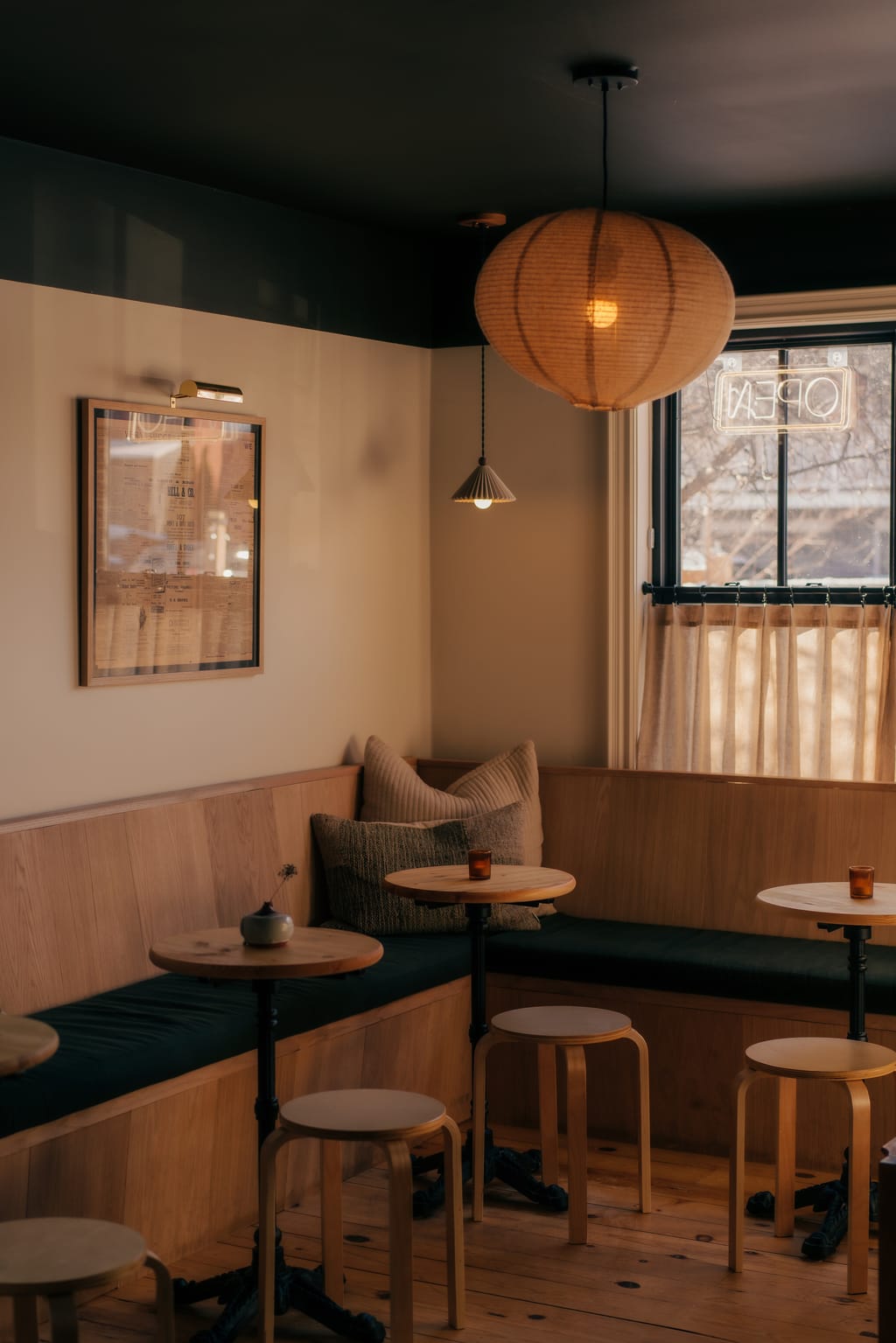 Wine bar corner with round wood tables, stools, a green banquette and an OPEN sign in the window