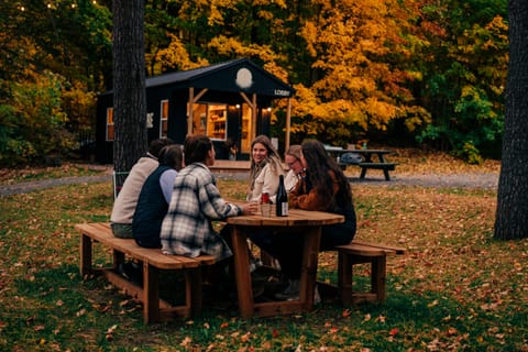 Friends sharing a bottle at a picnic table in front of a small cabin among autumn trees