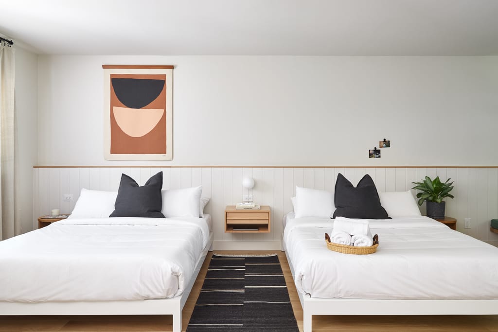 Room with two double beds, a terracotta and black wall hanging and a striped runner