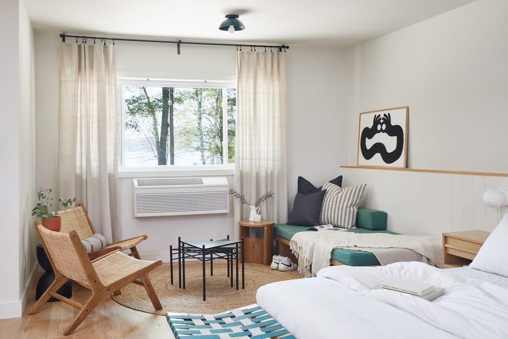 Guest room with a window onto the lake, rattan chairs, green daybed and a bed in the foreground
