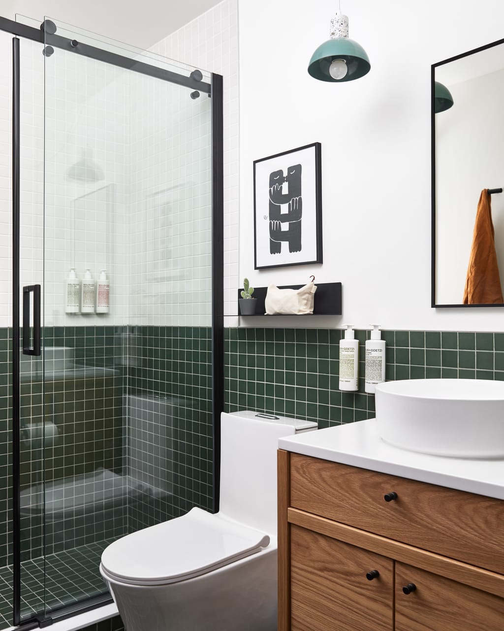 Bathroom with dark green tile, glass shower door, wood vanity and a round white sink