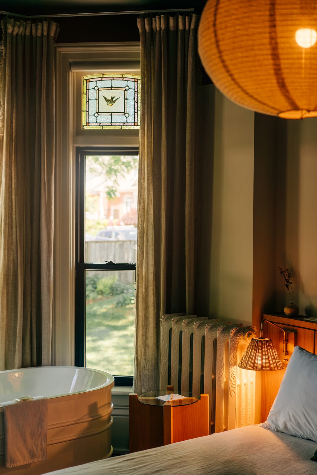 Bedroom corner with a stained-glass transom, linen curtains, a soaker tub and a radiator