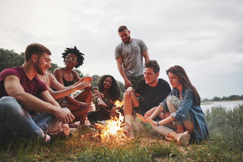 Friends gathered around a small campfire on the grass by a lake at dusk