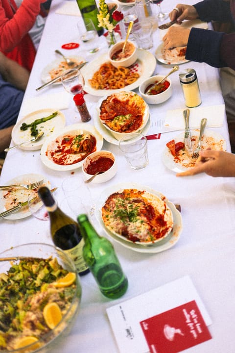 Long table set with pasta, baked dishes, salad and bottles after a shared meal