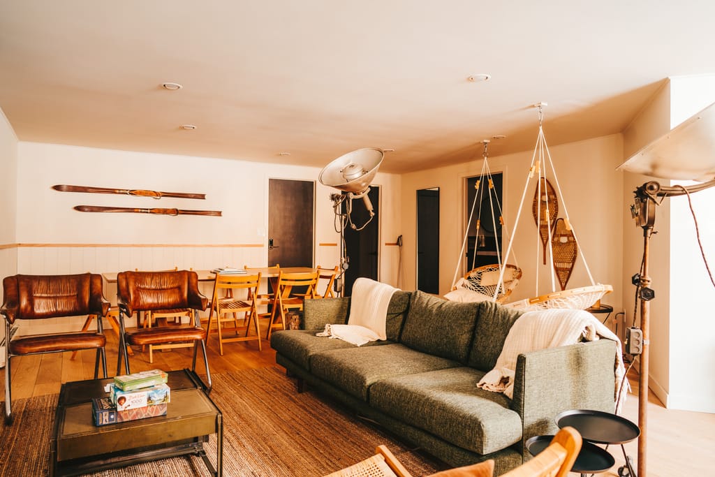 Lounge with a green sofa, leather chairs, vintage skis on the wall and a hanging chair