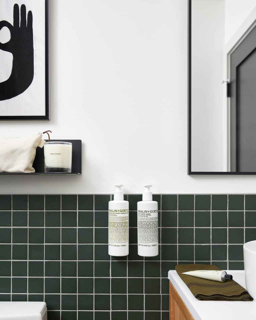 Two wall-mounted soap bottles on green tile beside a candle shelf and mirror