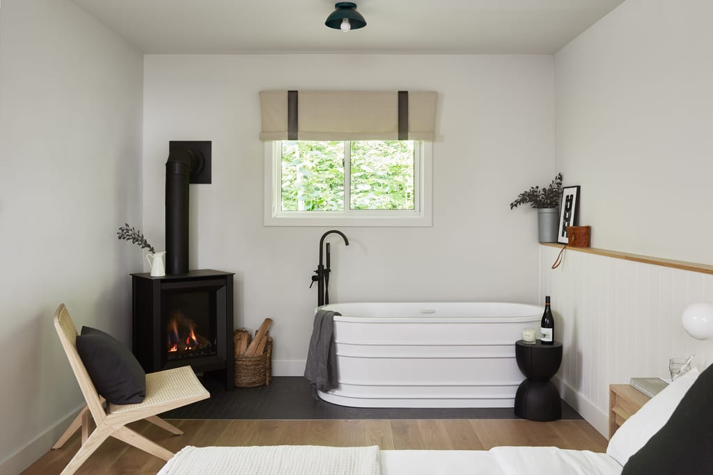 Bathroom with a freestanding white tub, a gas fireplace and a woven chair