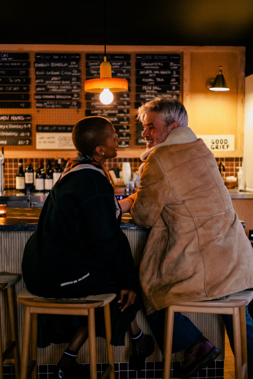 Two people chatting on stools at the wine bar counter under an orange pendant lamp