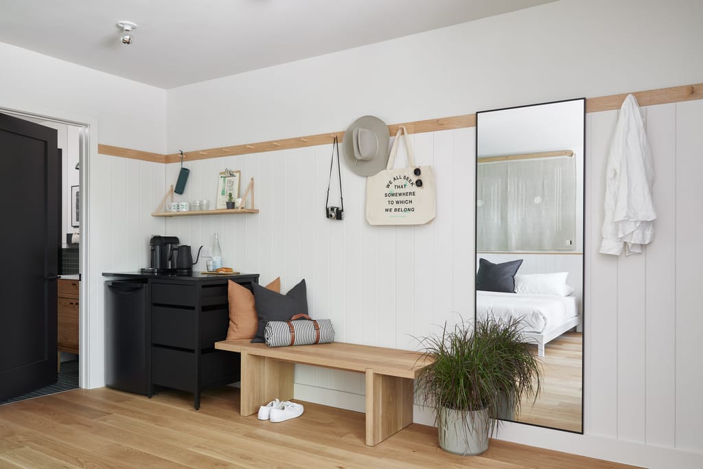 Room entry with coffee station, wood bench, full-length mirror and a tote bag on pegs