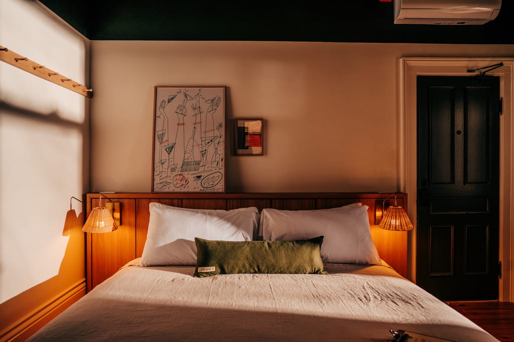 Double bed with a wood headboard, rattan sconces, framed line drawing and a dark door in warm light