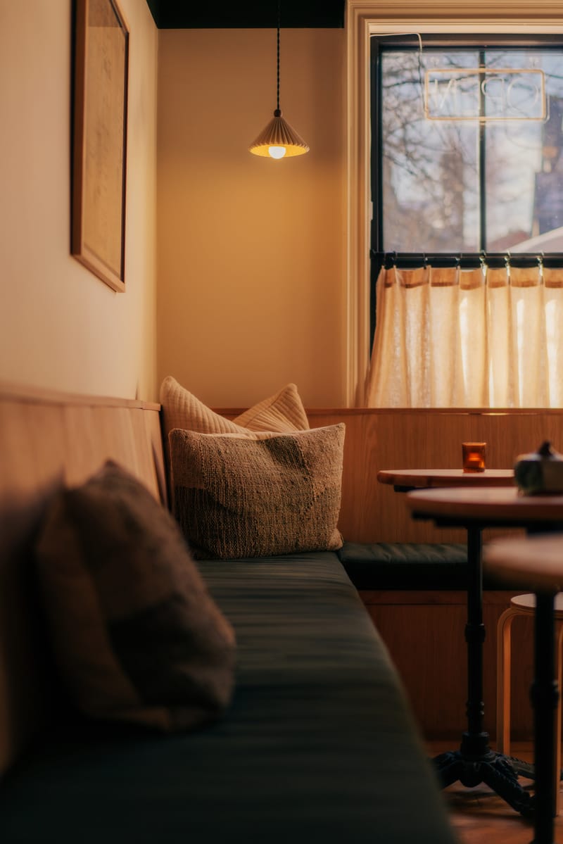 Cushioned banquette, small wooden tables and a pendant lamp at the wine bar under a window