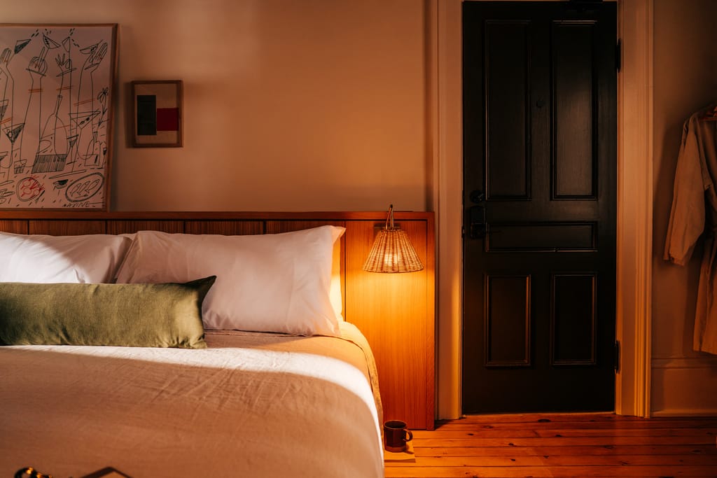 Guest room with a wood headboard, olive bolster, rattan lamp, a dark panelled door and a robe on a hook