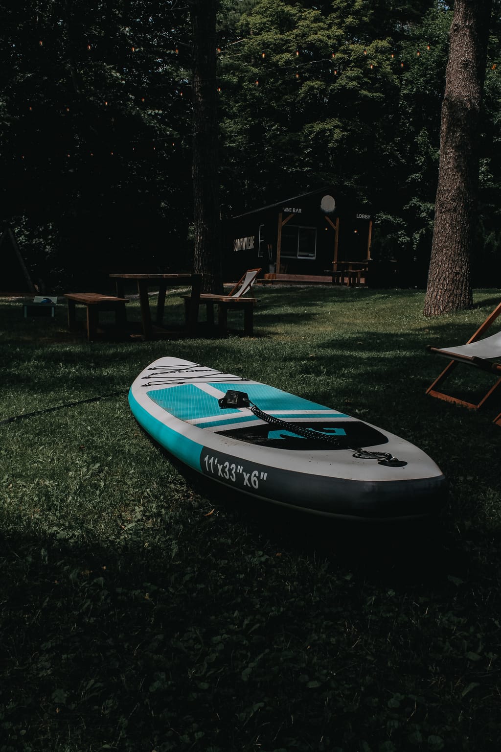 Inflatable paddleboard on the lawn with picnic tables and the black Lobby Wine Bar hut among trees