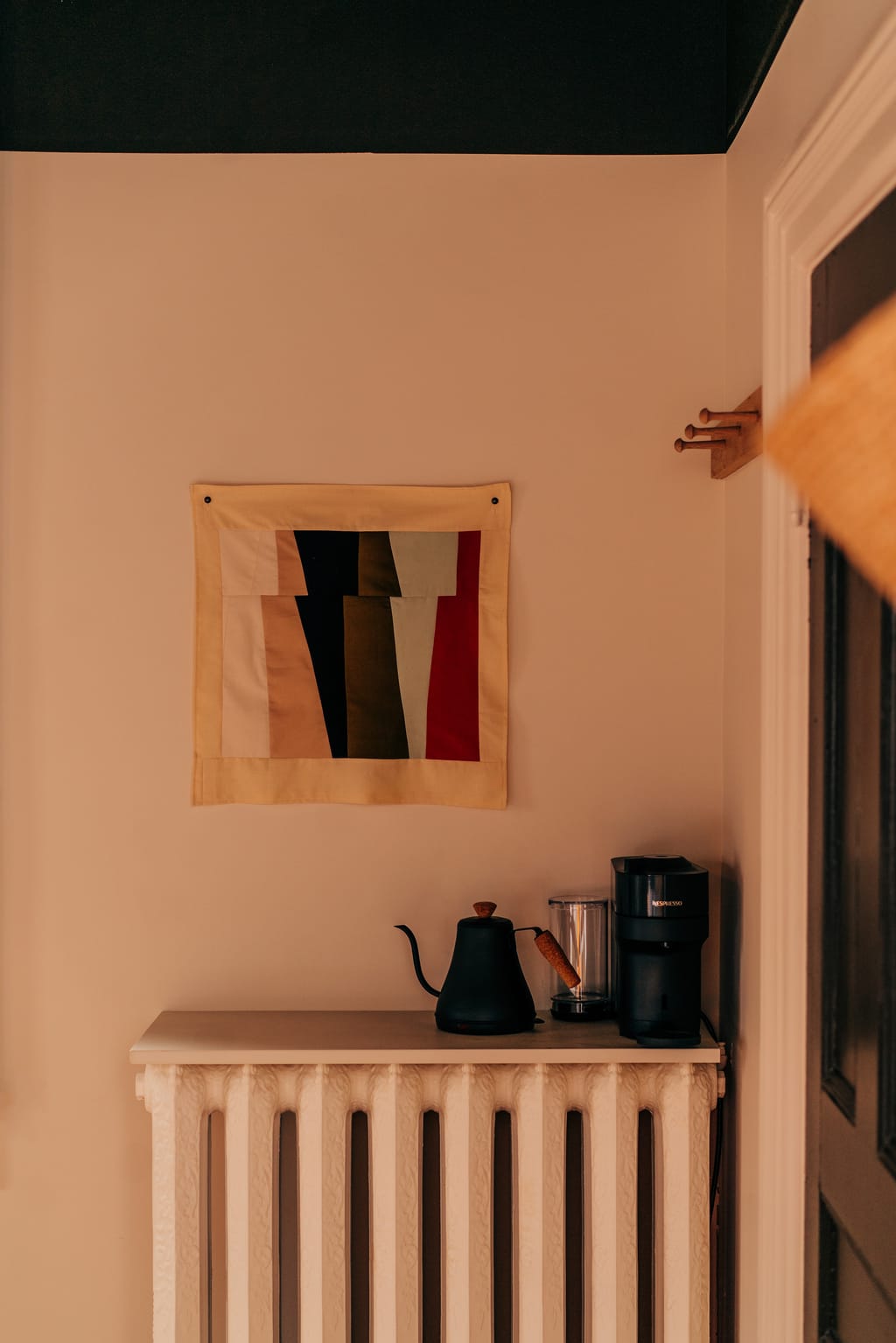 Kettle and coffee machine on a radiator shelf beneath a patchwork textile on the wall