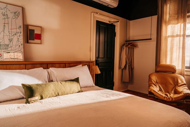 Bed with a green bolster pillow, framed art, a dark door and a robe on a rail
