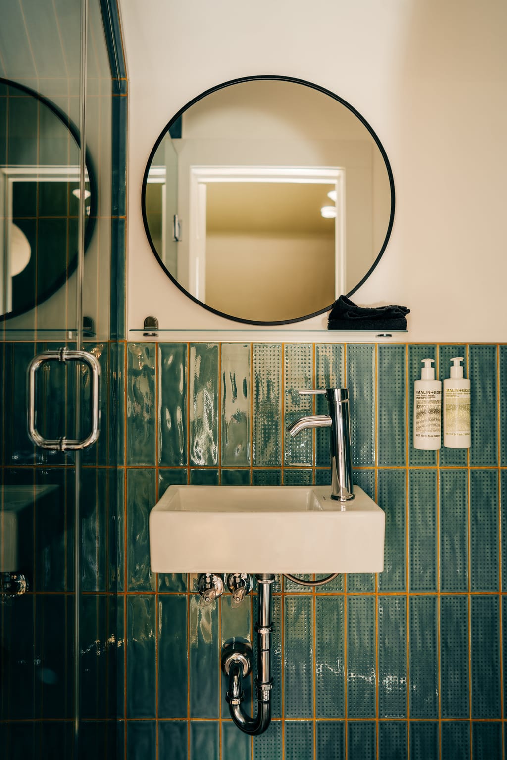 Green glazed tile wall with a small wall-mounted sink, round mirror and hand soap