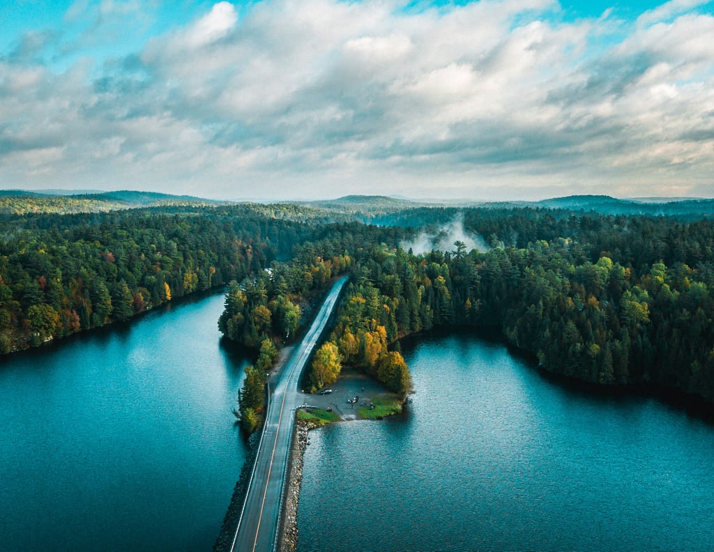 Aerial view of a road crossing a narrow strip between two lakes in autumn forest