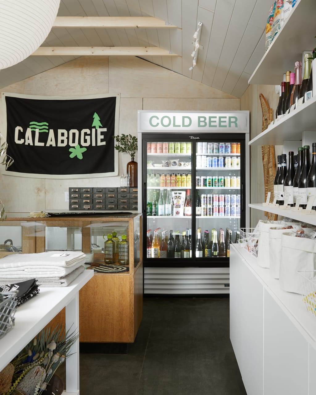 Small shop with a Calabogie flag, a cold beer fridge, wine shelves and folded linens
