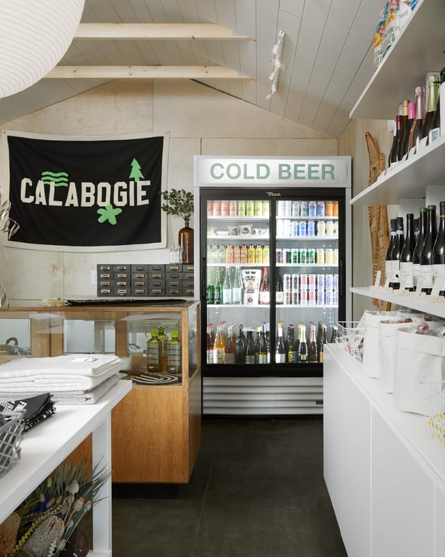 Small shop with a Calabogie flag, a cold beer fridge, wine shelves and folded linens