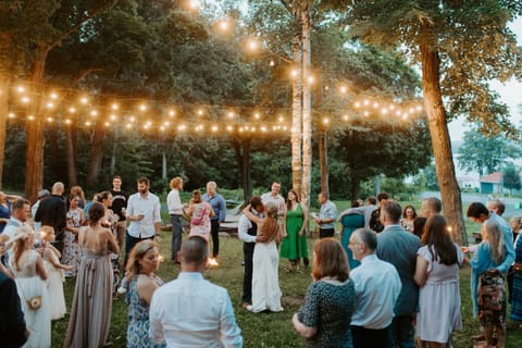 Wedding guests gather on a lawn under strings of lights as a couple dance at dusk