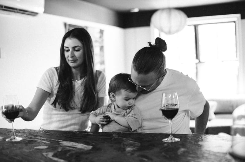 Couple with a toddler and two glasses of red wine at a stone bar, in black and white