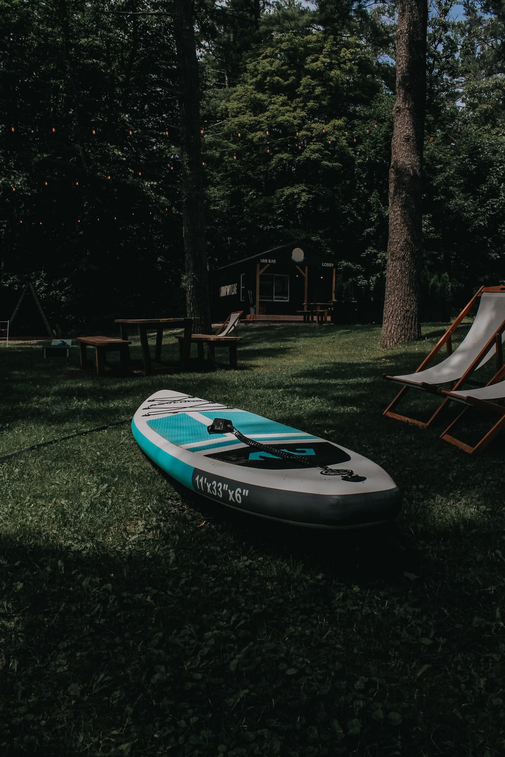 Inflatable paddleboard on the lawn with sling chairs, and the Lobby wine bar cabin among the trees