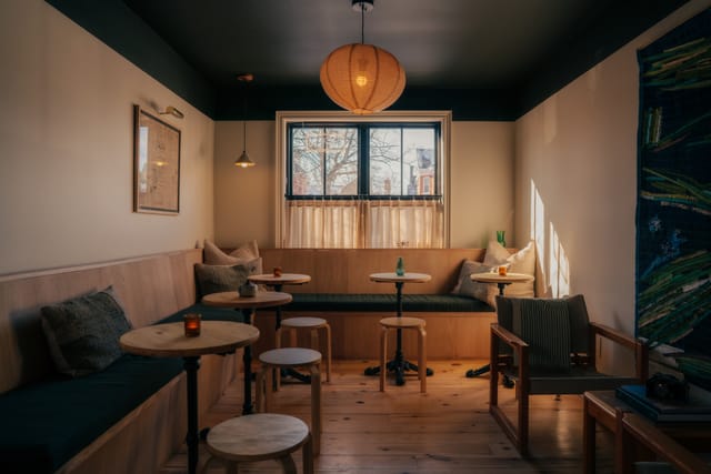Lounge with a built-in banquette, small round tables and a paper lantern by the window