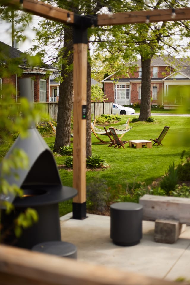 Garden with a fire table under a timber pergola, hammock and chairs on the lawn