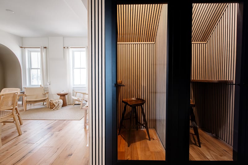 Two slatted-wood focus booths with dark stools behind glass doors, a bright room with a rattan chair beside them