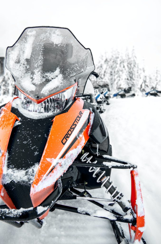 Credit: Yves Scheuber Unsplash, Snowmobiles lined up on a snowcovered trail with trees in the background
